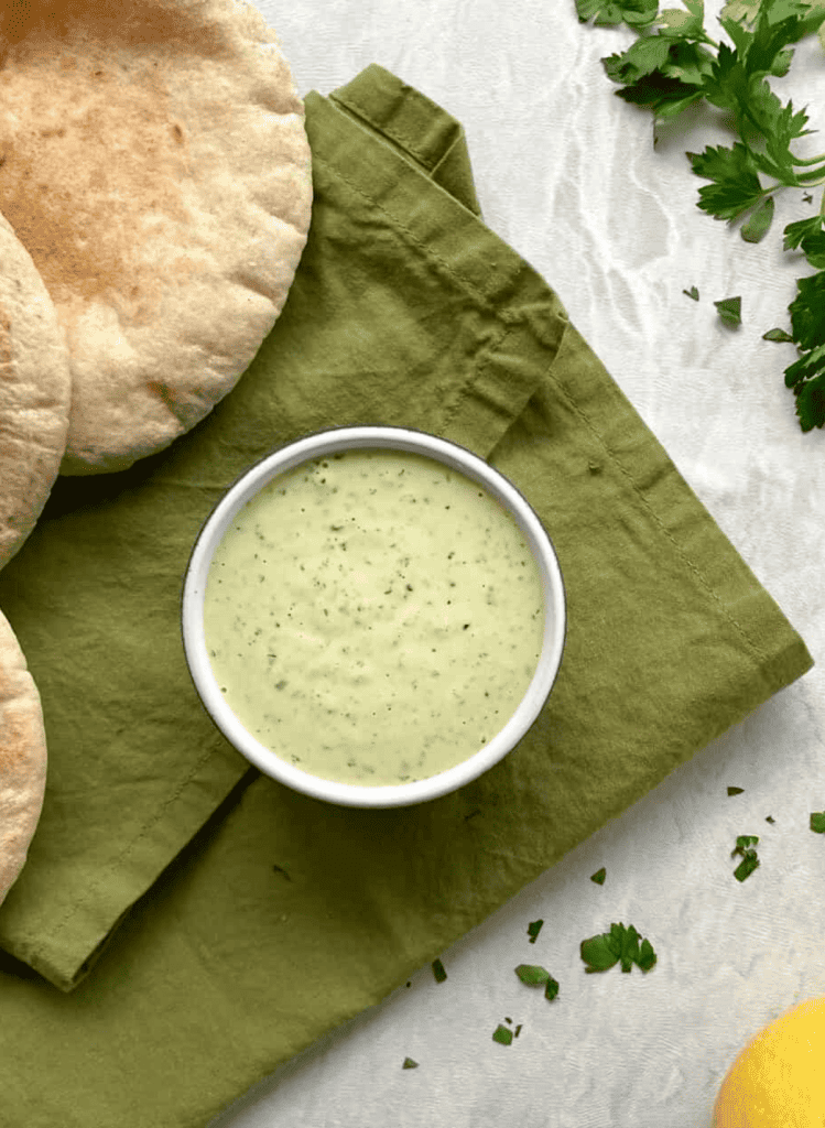 Lemon Herb Dip in a white bowl with pita rounds and green towel in the background