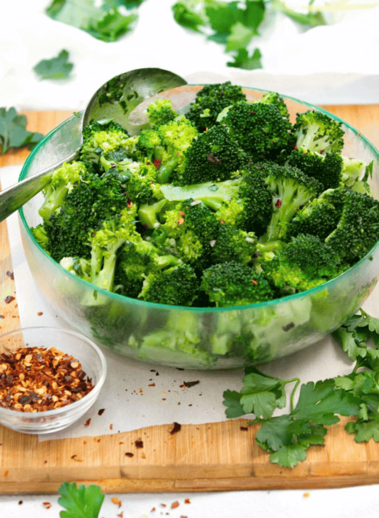 chimichurri broccoli salad in a glass bowl and a small bowl of red chili flakes on the side