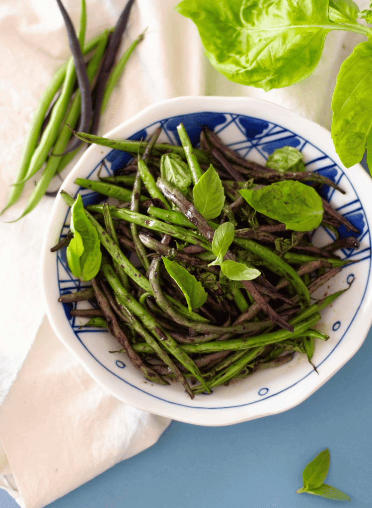 Sauteed green beans with basil in a white and blue bowl with a white towel in the background