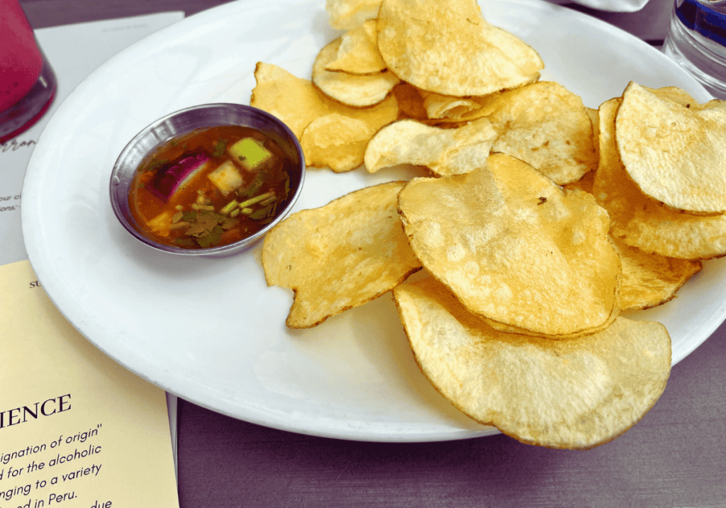 Potato chips and a small silver ramekin of watery tomato sals on a white round plate