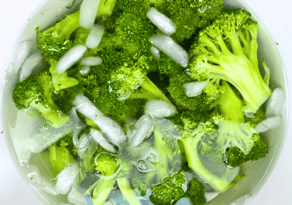 Broccoli florets in a white bowl of ice water