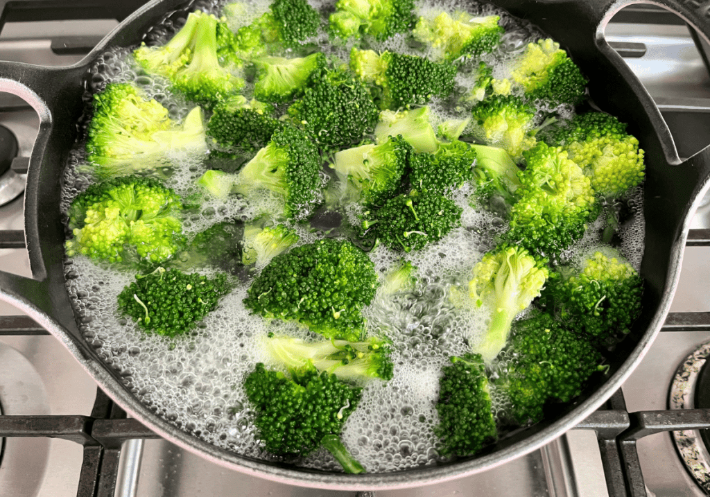 Broccoli florets cooking in boiling water in a round pot.