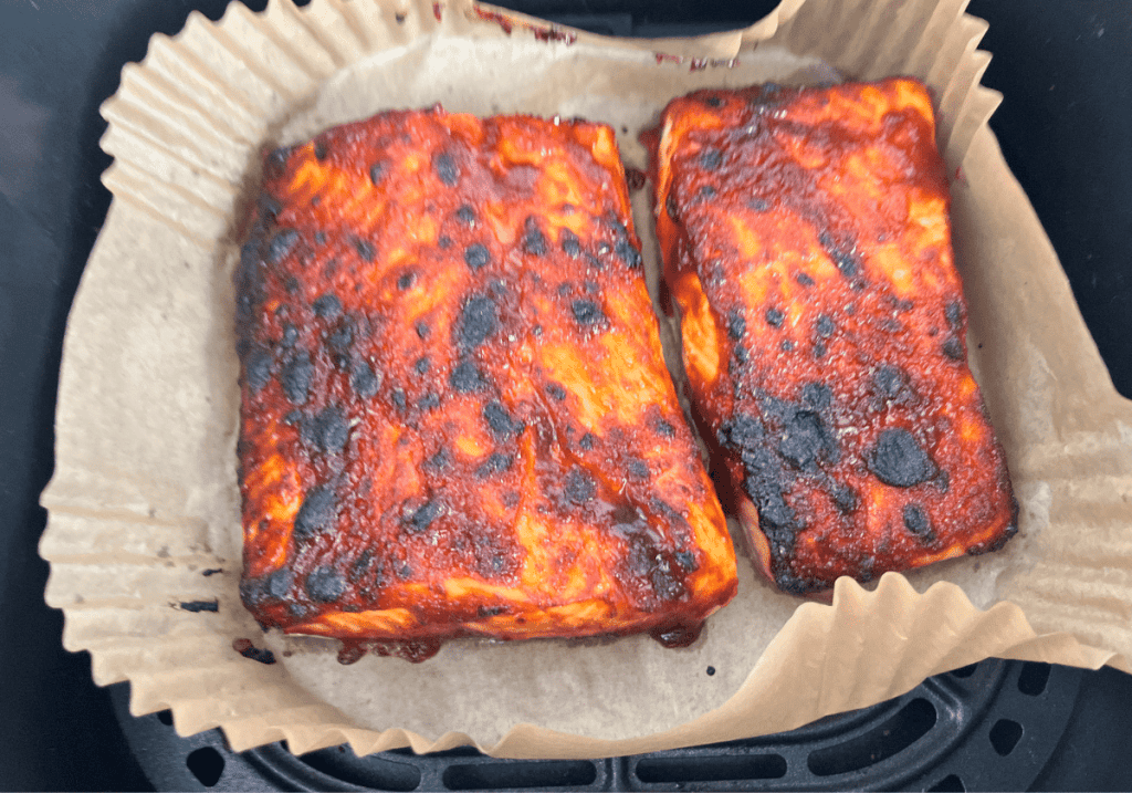 Two pieces of baked Hawaiian salmon in an air fryer basket on parchment paper.