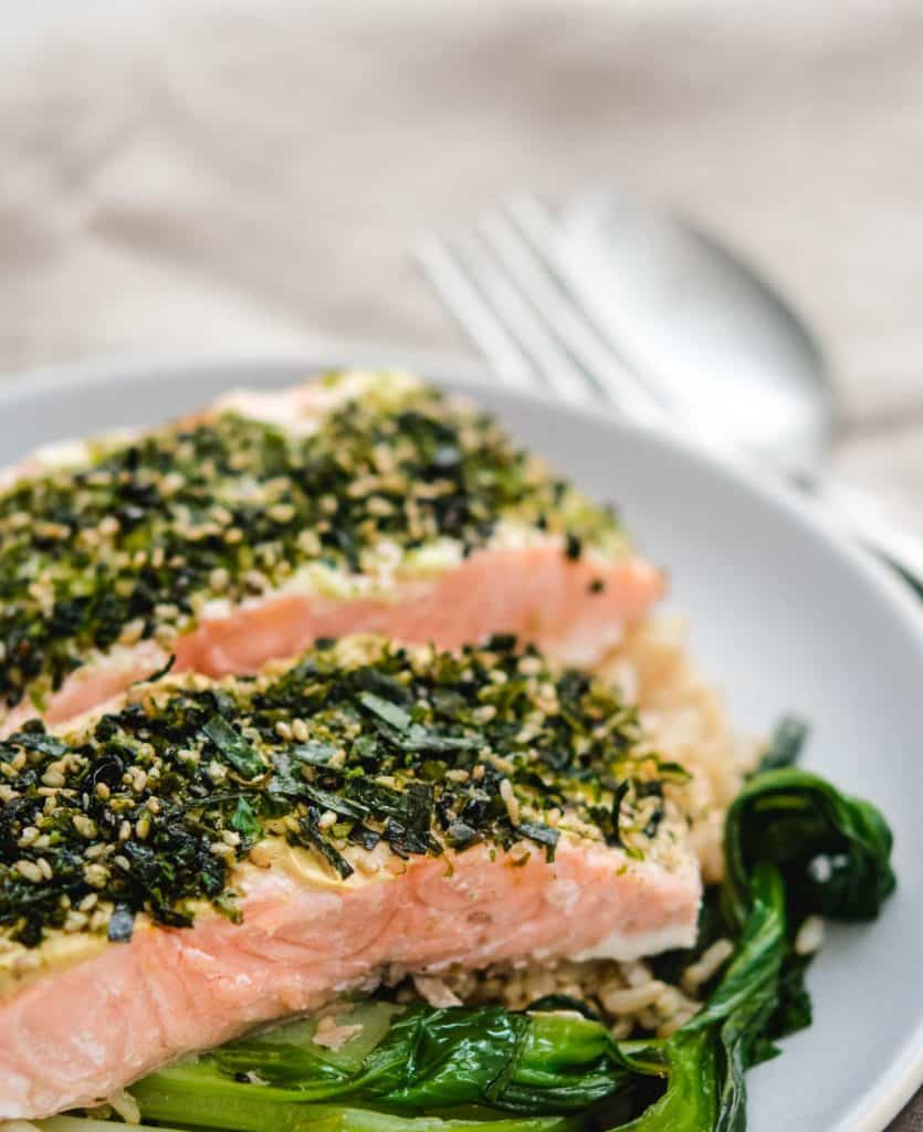 Two fillets of furikake salon on a gray plate with bok choy and a fork and spoon next to the plate.