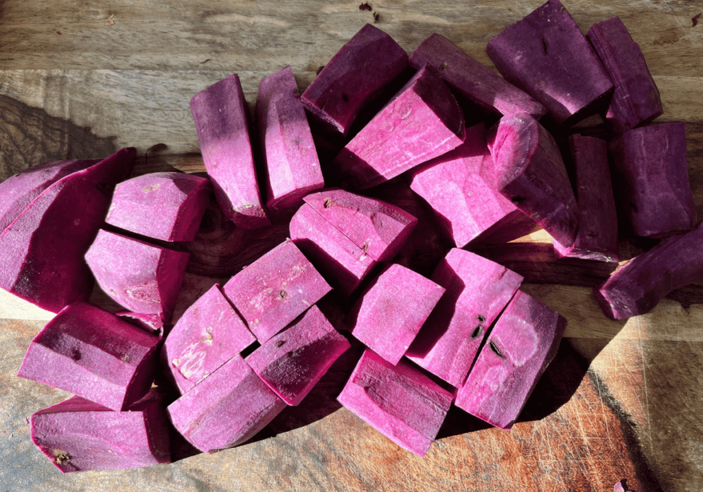 Purple potato cut into chunks on a wooden cutting board.