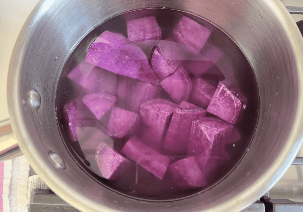 Raw purple potato chunks in a silver saucepan covered with water.
