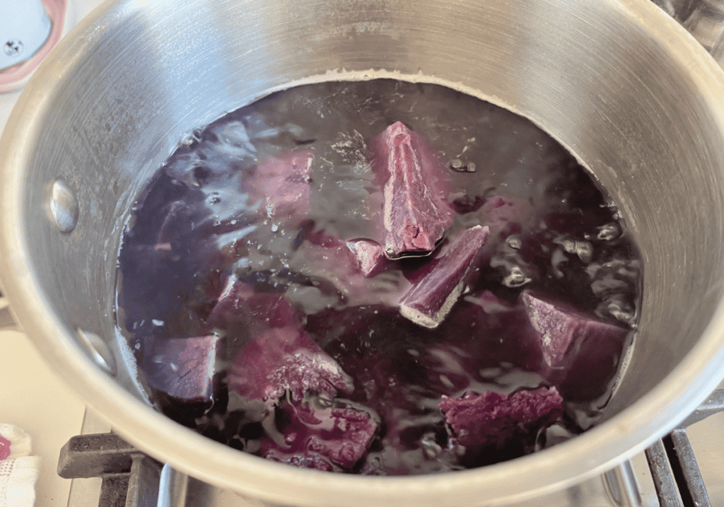 Purple potatoes cooking in boiling water in a silver saucepan.