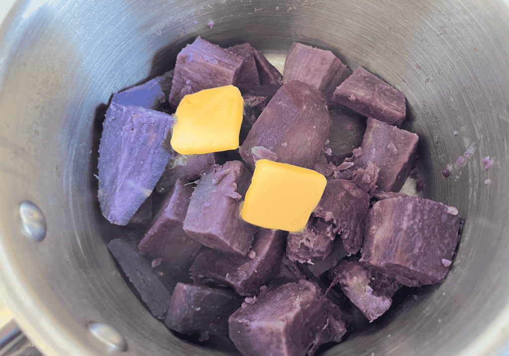 Cooked purple potato chunks in a sauce pan with two dabs of butter.