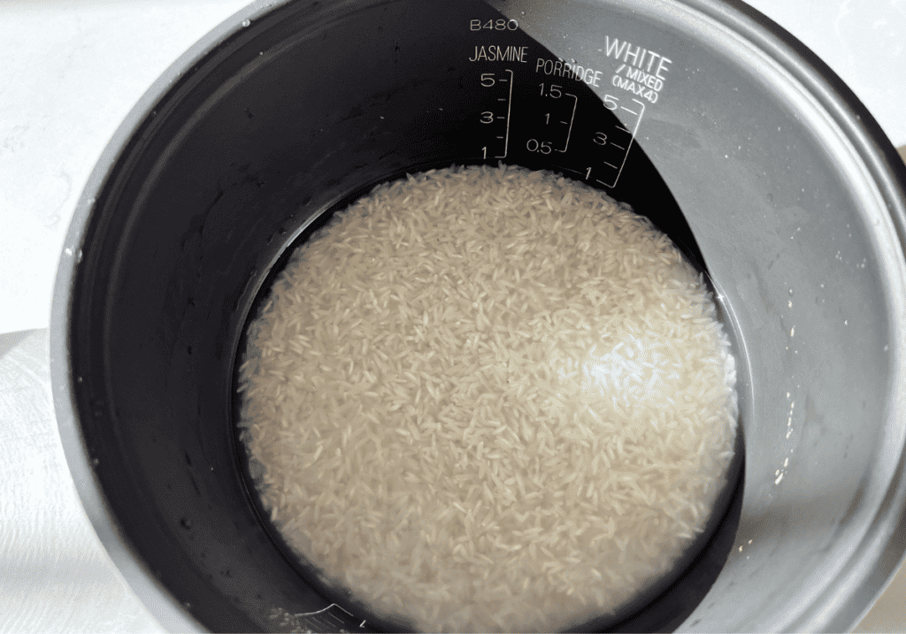 Jasmine rice in water in a rice cooker pot.
