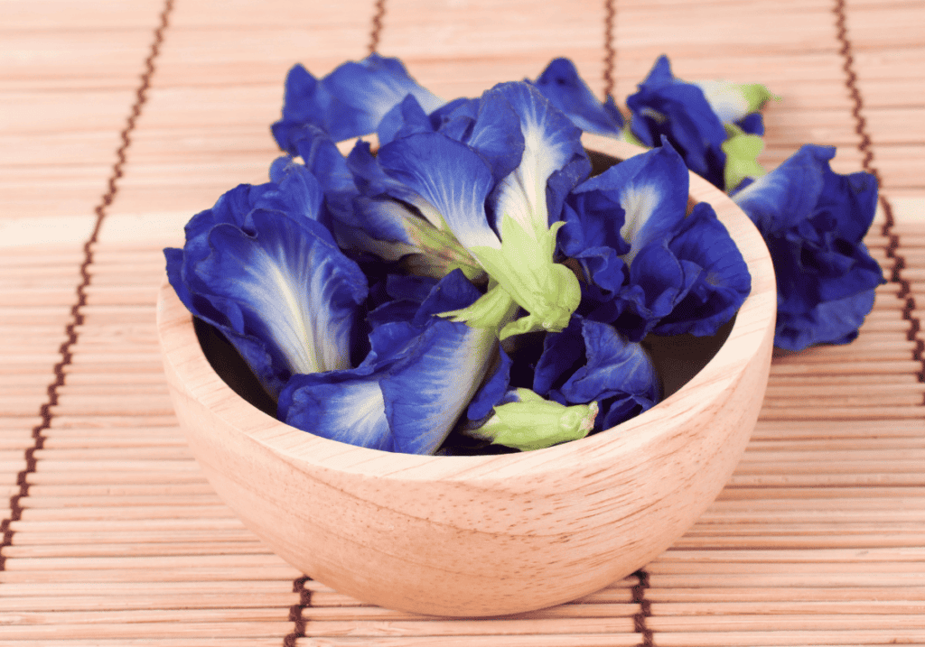 Fresh butteryfly pea flowers in a wooden bowl on a bamboo slat background