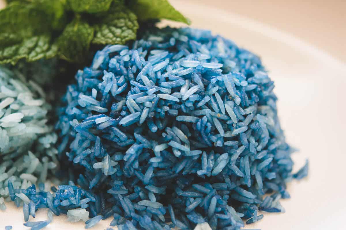 A scoop of dark blue butterfly pea flower jasmine rice on a white plate with mint leaves in the background.