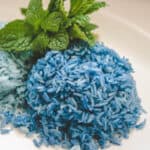 2 scoops of blue butterfly pea flower jasmine rice on a white plate with mint garnish