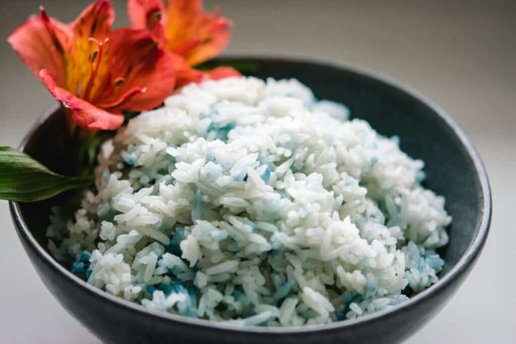 Butterfly pea flower rice in a gray bowl with an orange flower garnish.