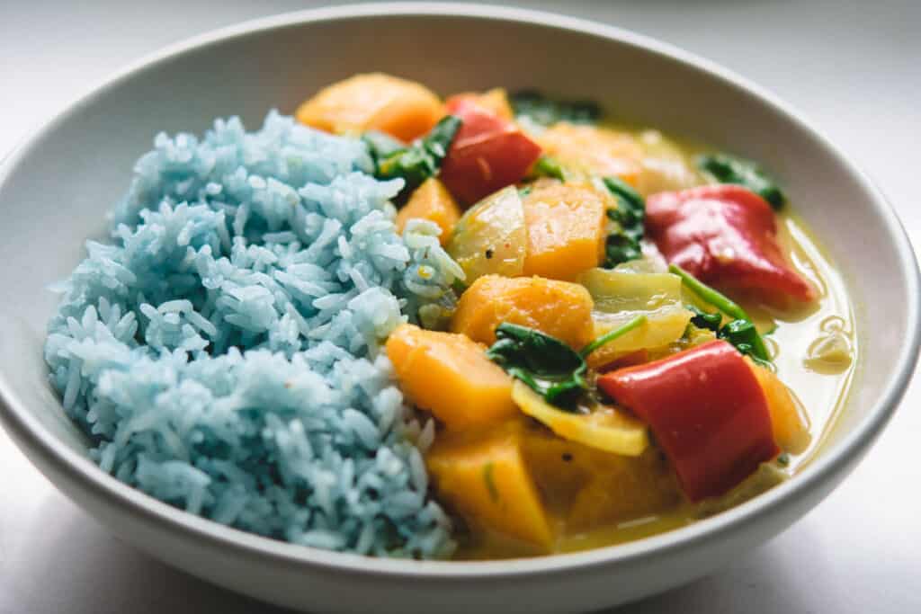 A white plate filled with half butterflower pea rice and half butternut squash curry.