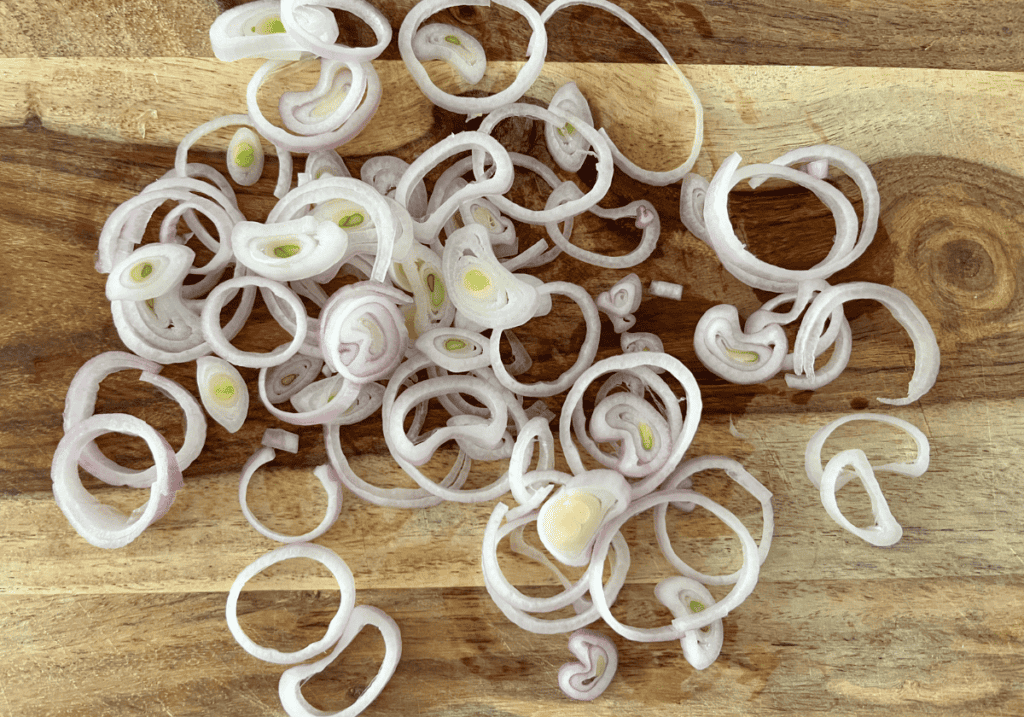 Sliced shallots separated into a rings on a wooden cutting board