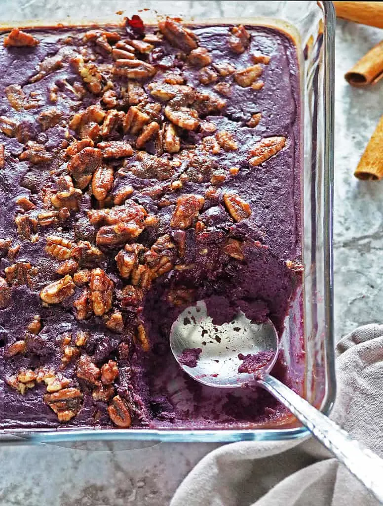 A glass baking dish of purple sweet potato souffle with pecans on top