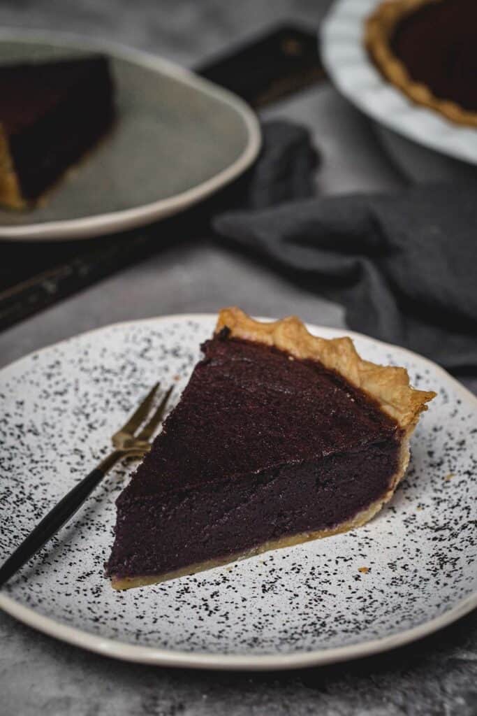 A slice of purple sweet potato pie on a white plate with speckles and a fork