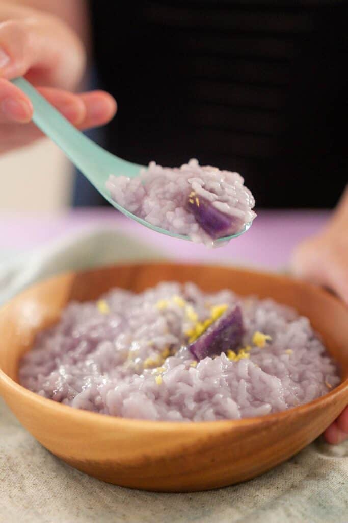 A spoonful of purple sweet potato congee over a wooden bowl of purple sweet potato congee.