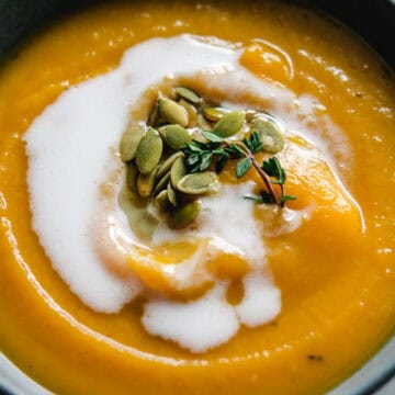 Butternut squash apple soup in a gray bowl with coconut milk, pumpkin seeds, and fresh thyme garnish
