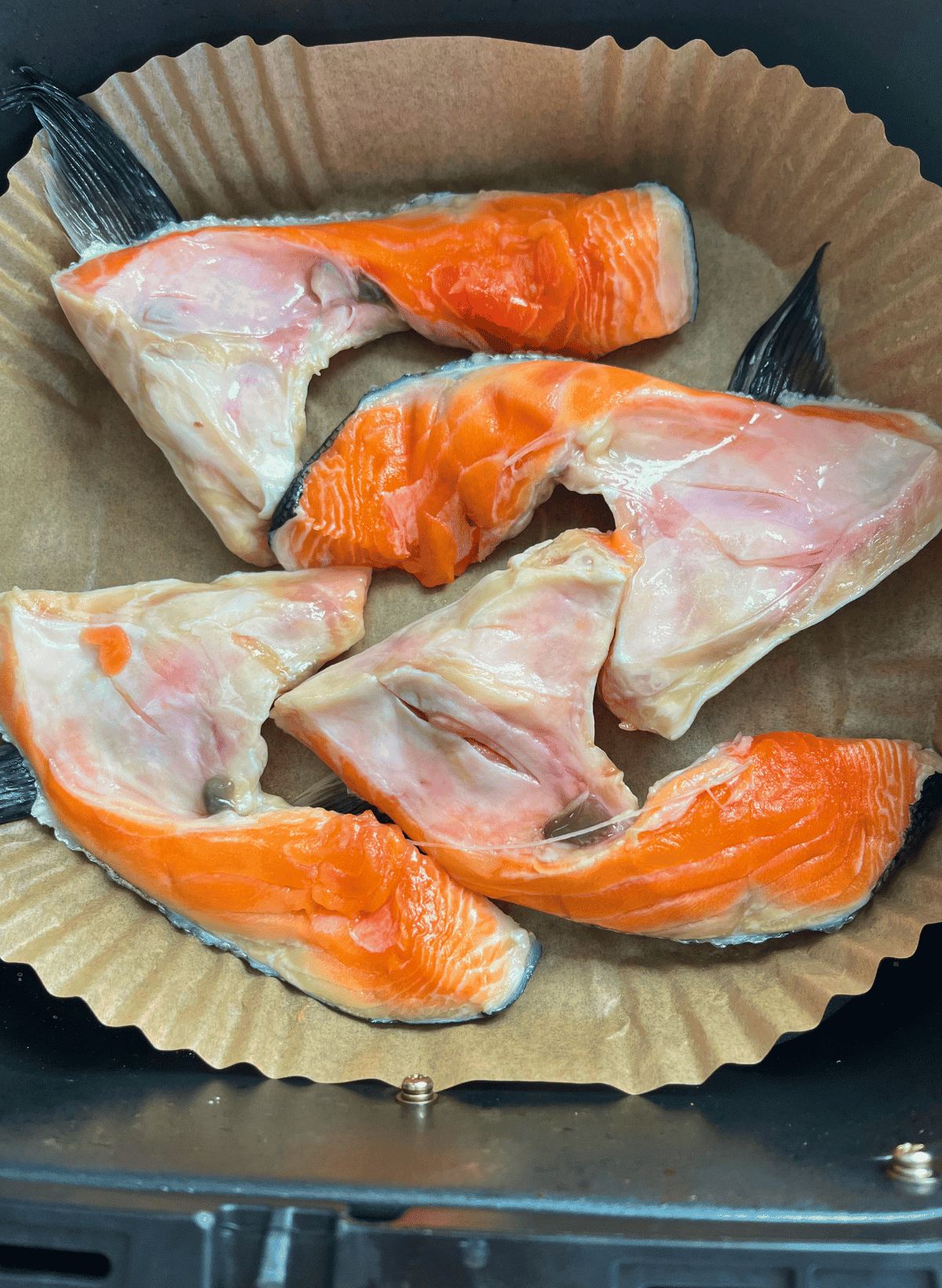 Raw salmon collars on parchment paper in a black air fryer basket
