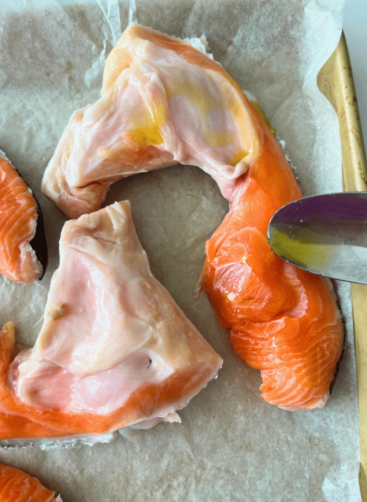 Salmon collar with olive oil and a silver spoon on a parchment lined gold baking sheet