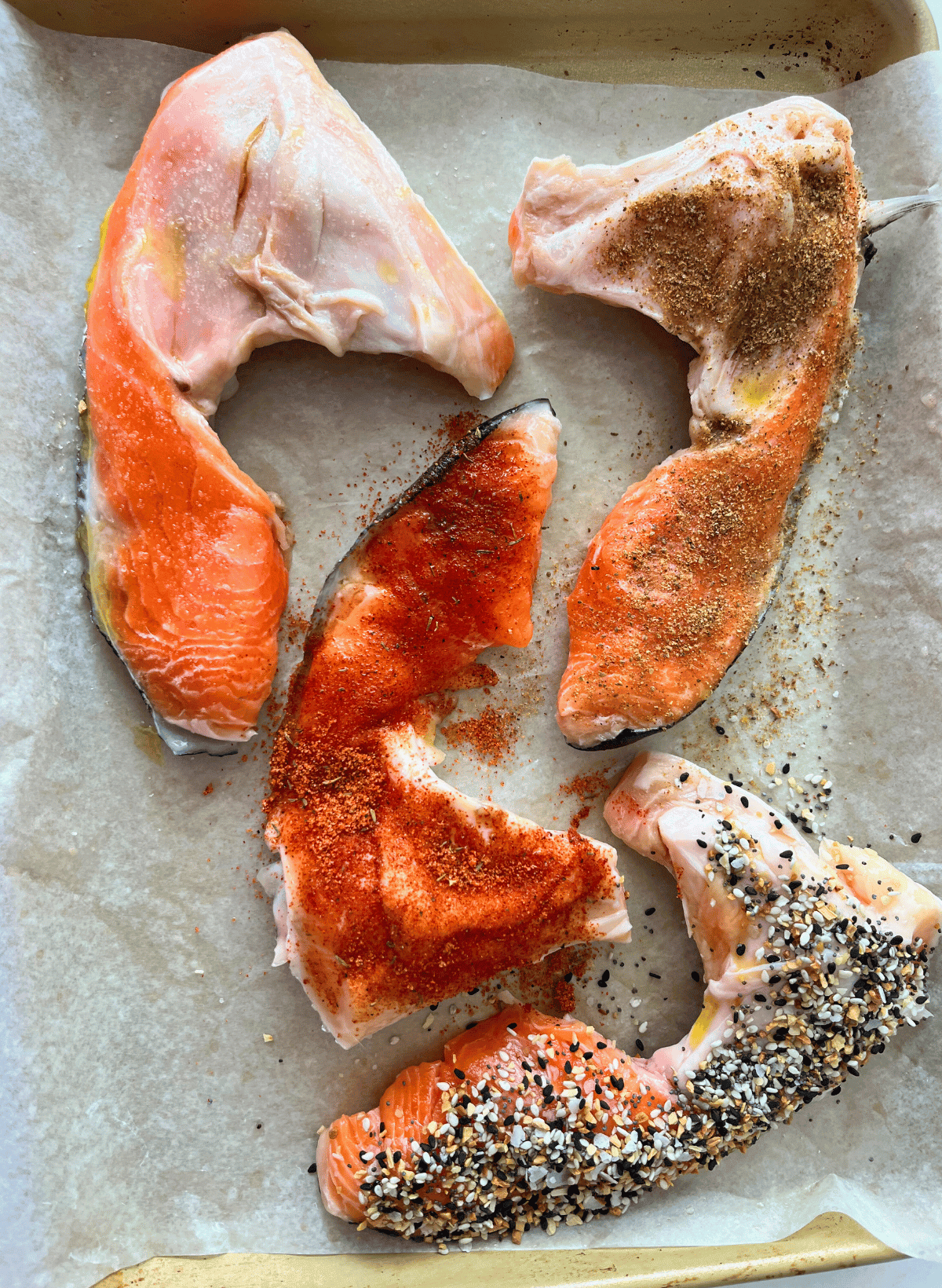 Raw salmon collars with different toppings on a parchment lined baking sheet