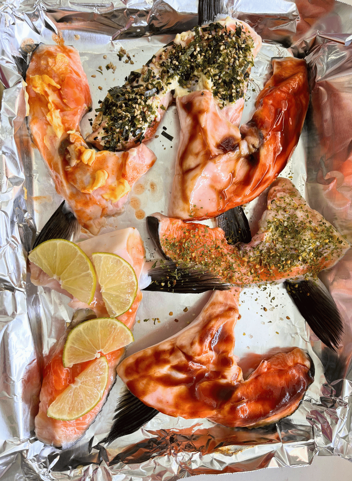 Raw salmon collars with a variety of toppings on a foil lined baking sheet