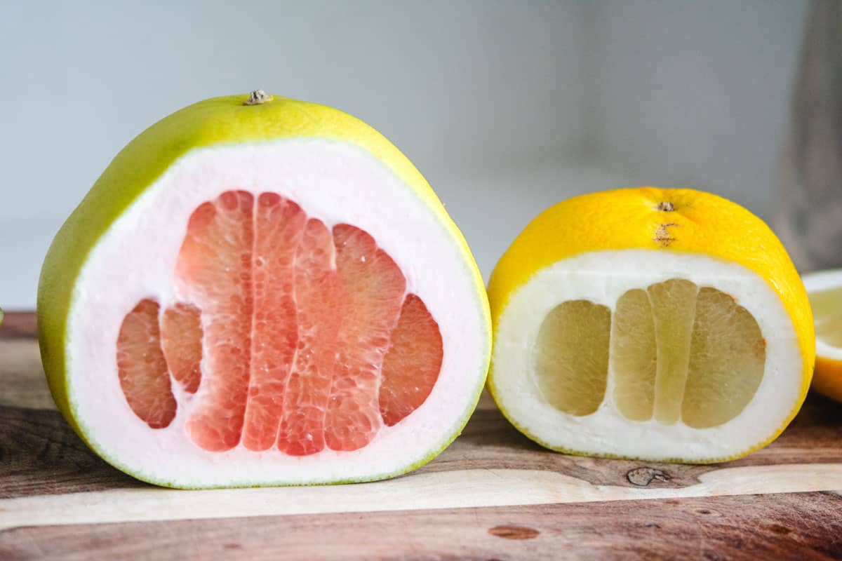 A pink and yellow pomelo cut in haf on a wooden cutting board