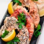 4 salmon collars with different toppings on a rectangular black plate with parsley garnish and lemon wedges