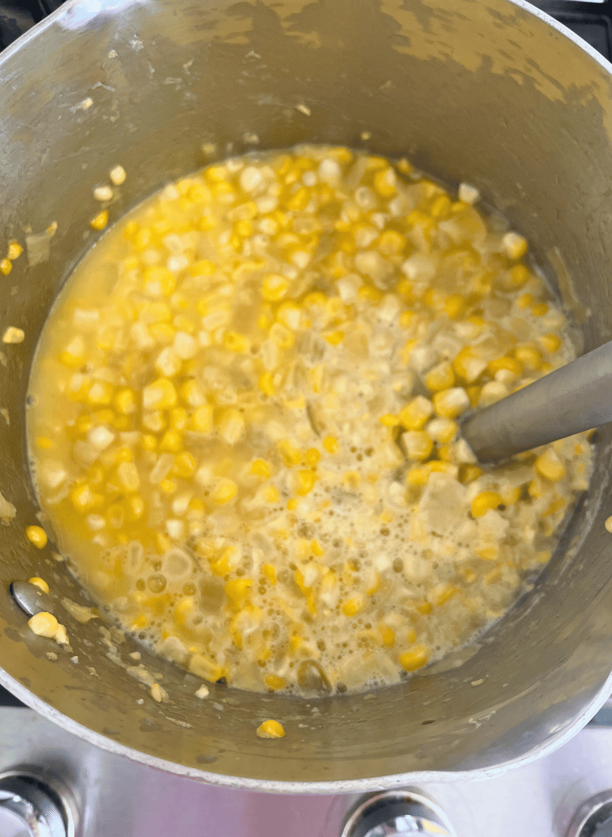 corn soup being pureed with an immersion blender stick in a silver saucepan