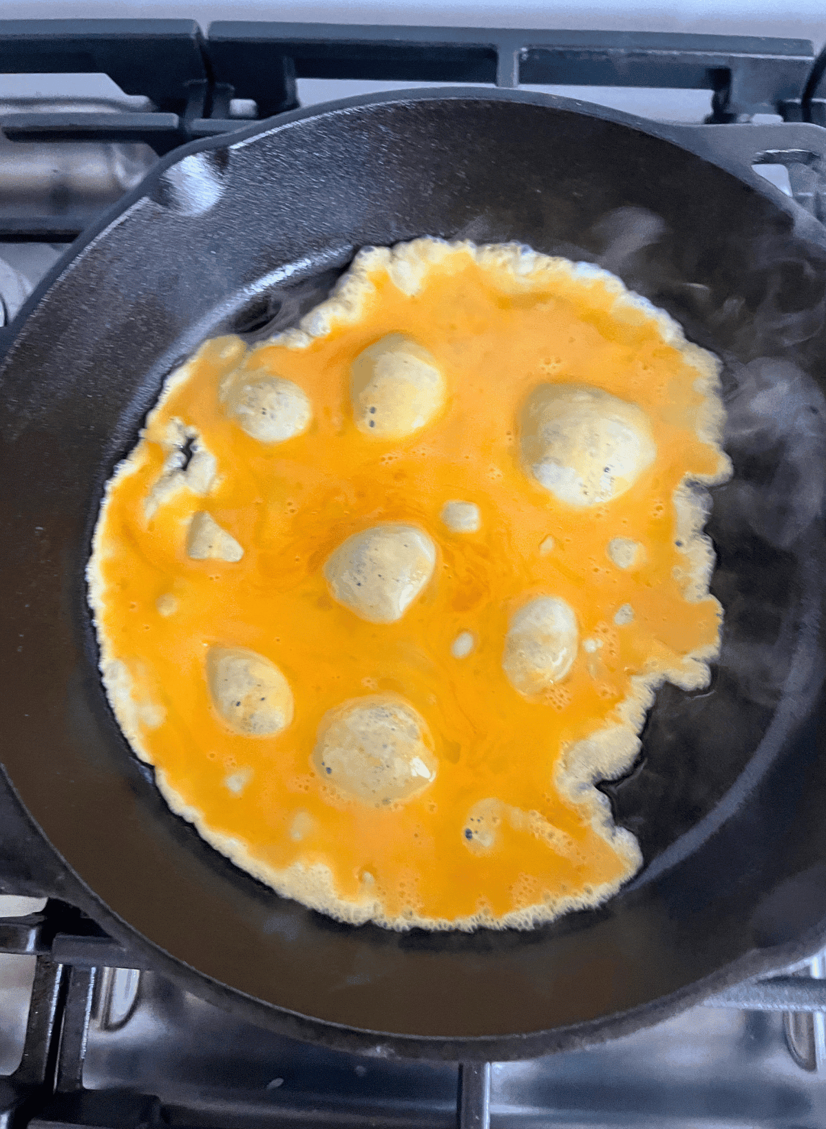 a thin layer of scrambled eggs bubbling in a cast iron pan