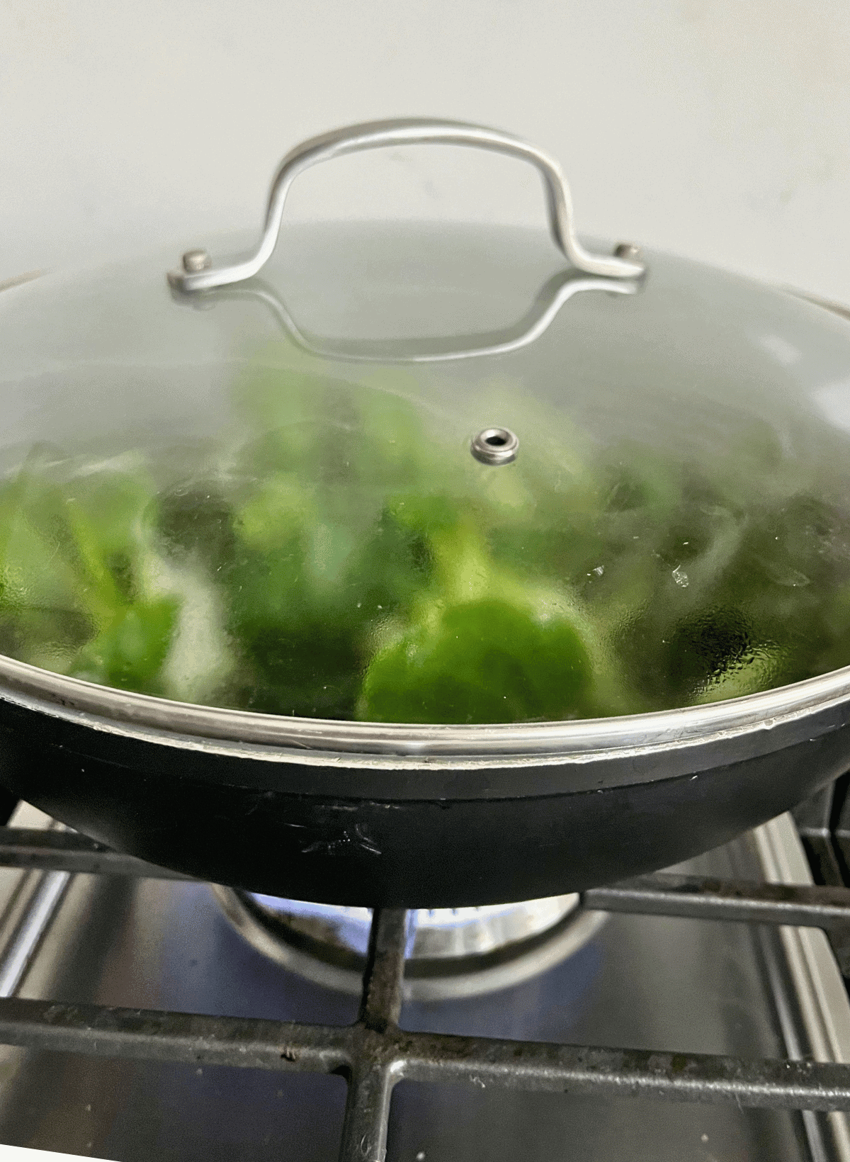 raw bok choy in a gray wok with a glass over on a burner
