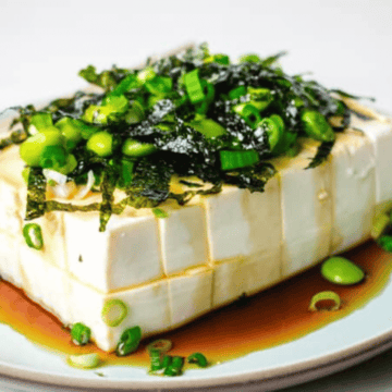 Japanese tofu salad on a round blue plate with seaweed strips, edamame, and sliced green onion