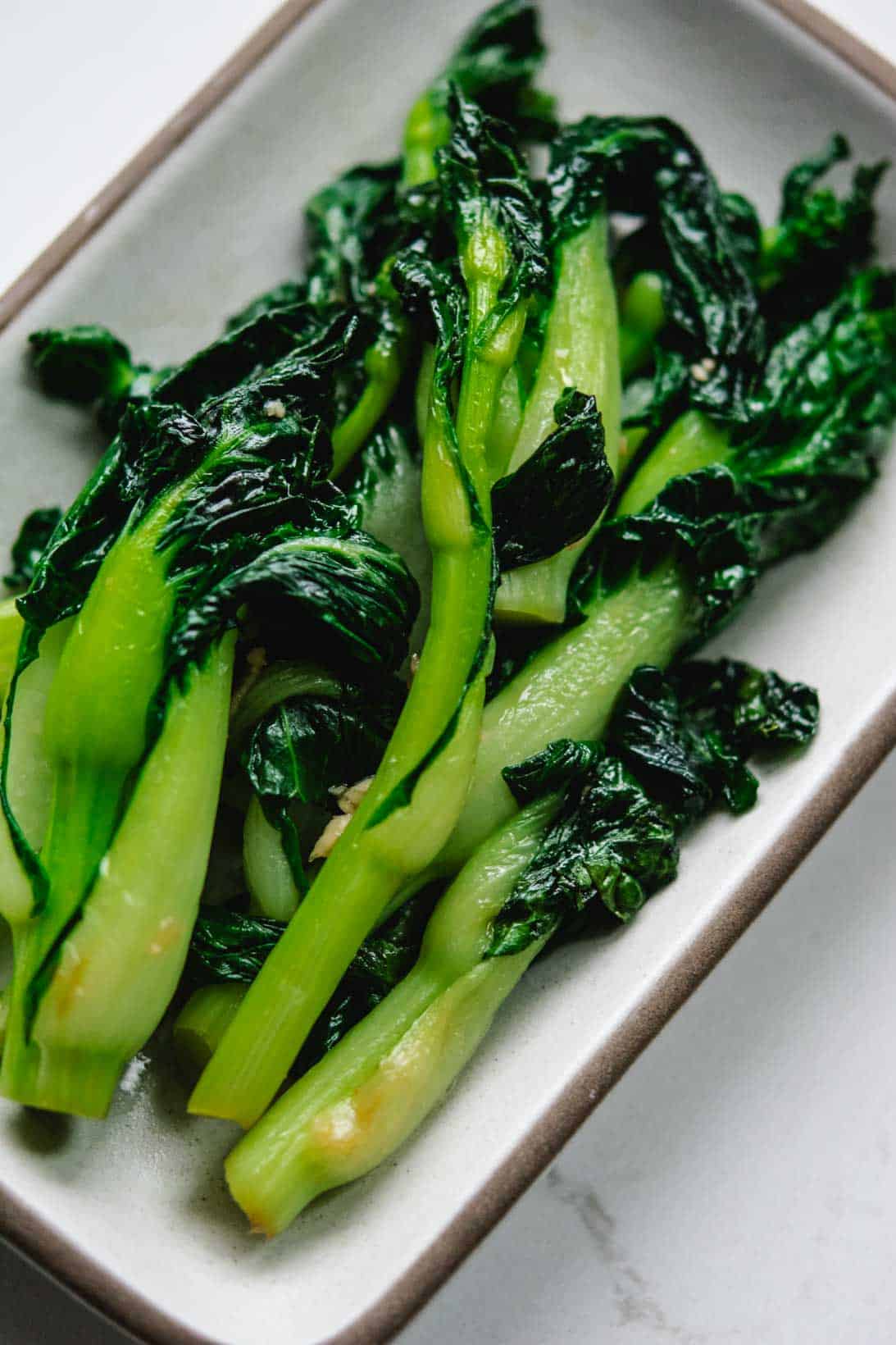 stir fried baby book choy on a white rectangular plate