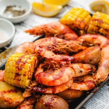 Head on shrimp with boiling crab sauce and corn on the cob on a white newspaper background