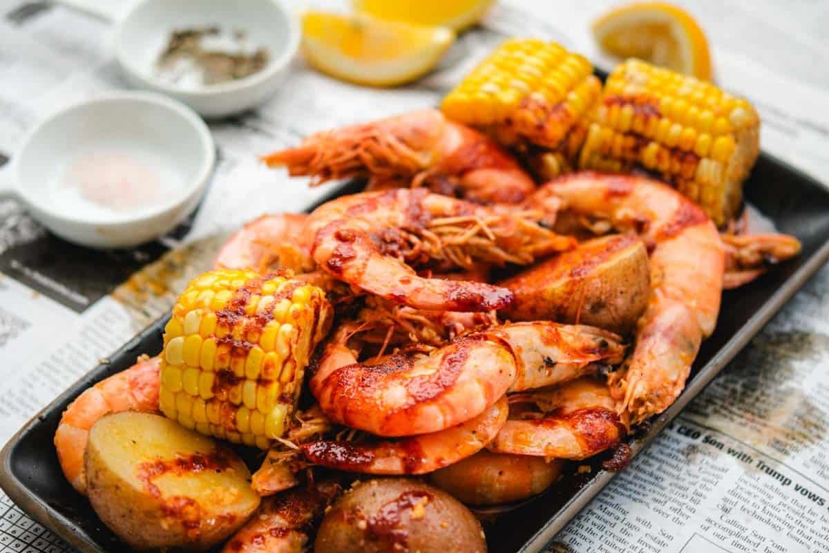 Head on shrimp with boiling crab sauce and corn on the cob on a white newspaper background