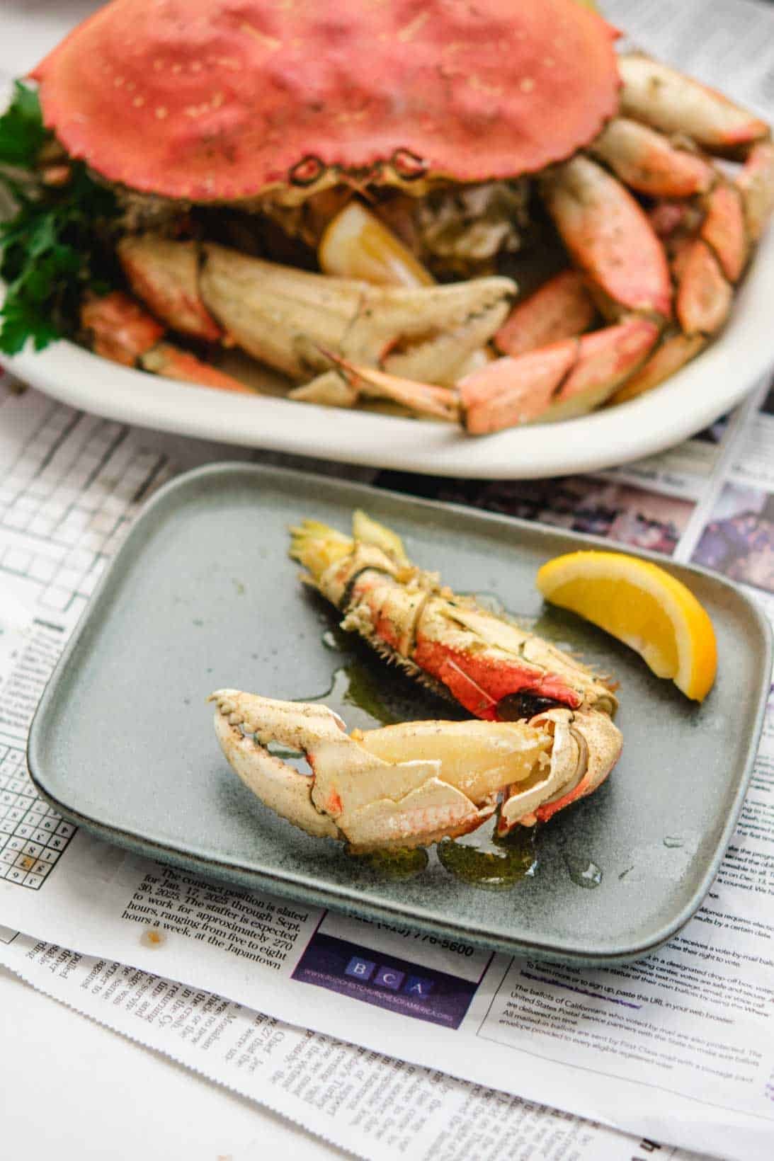 cracked crab claw on a grey rectangular plate with a lemon wedge and whole Dungeness crab in the background