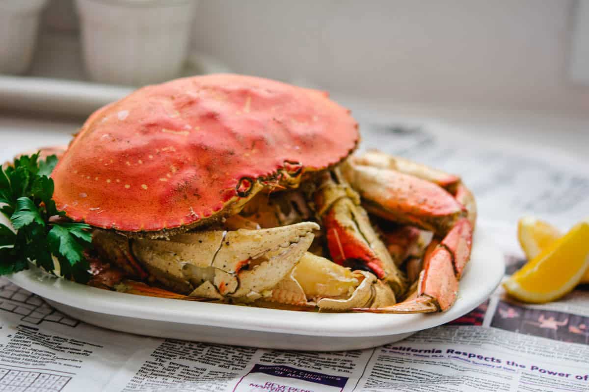 Dungeness crab with cracked legs one a white plate and Thanh Long butter sauce