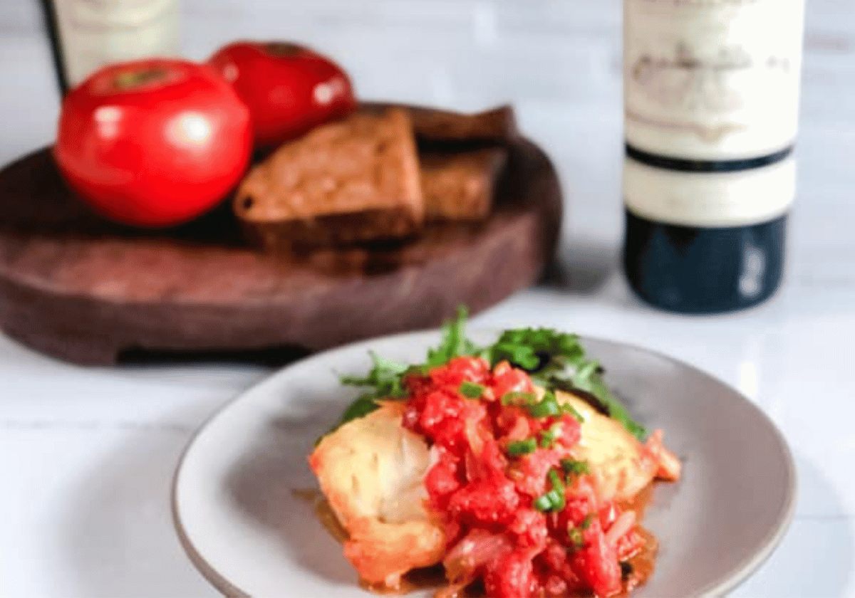Vietnamese fried fish on a gray plate with bread, wine, and tomatoes in the background