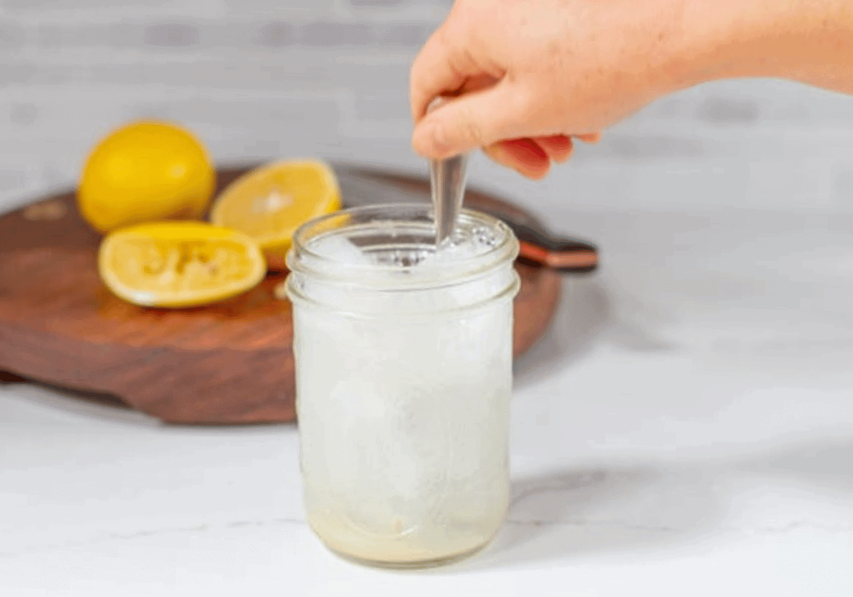 hand stirring a silver spoon in a mason jar of Vietnamese lemon soda chanh with cut lemons in the background