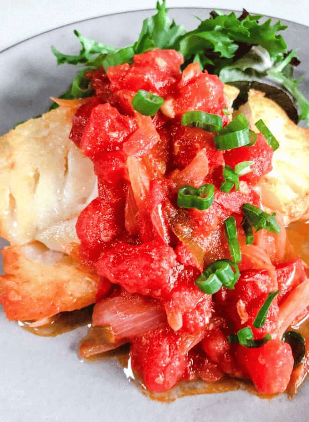 Vietnamese fried fish with tomato sauce on a gray plate with green salad