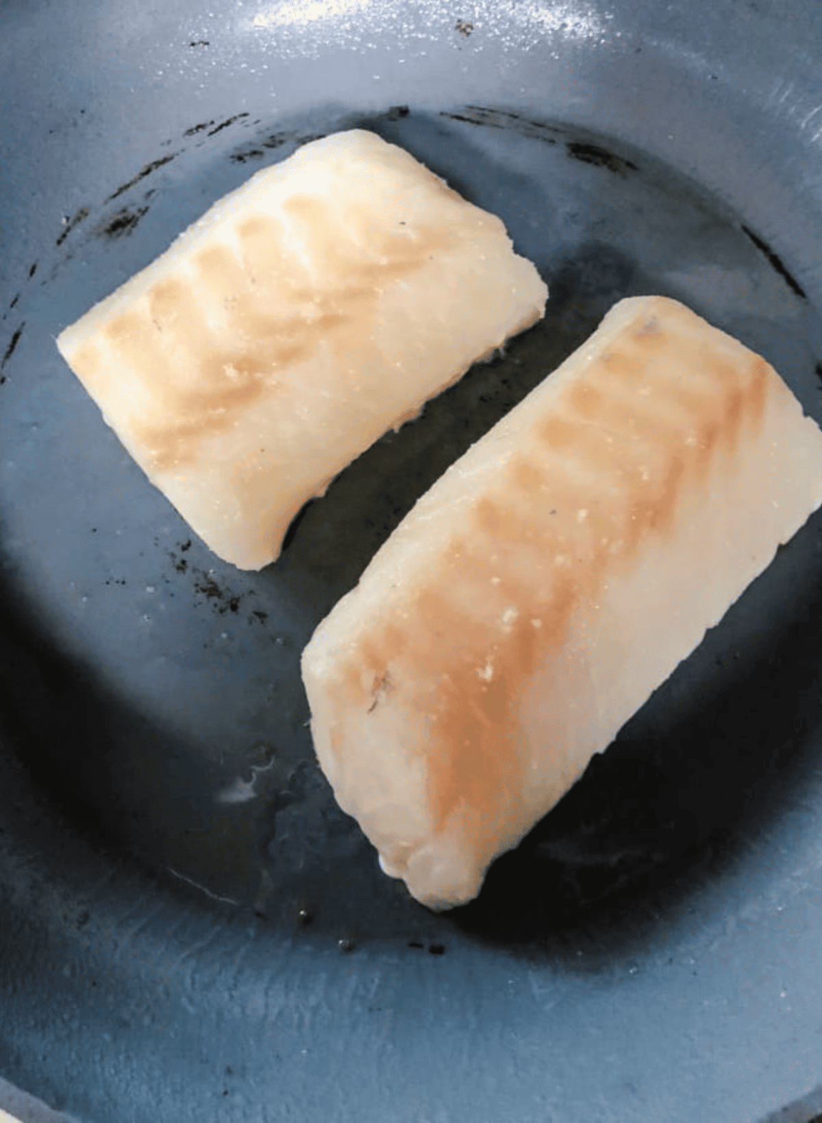 2 pieces of cod filets being cooked in a silver pan