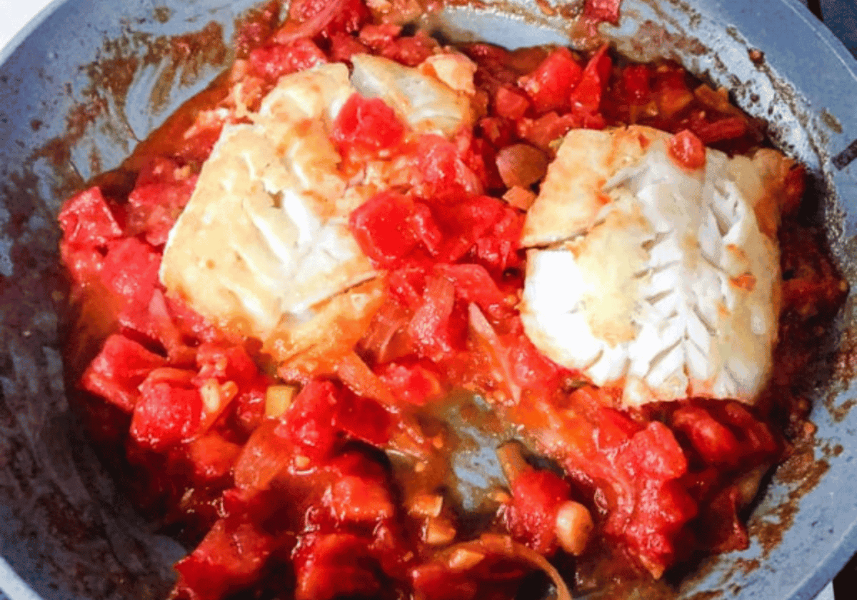 2 cooked cod filets in a silver pan with tomato sauce