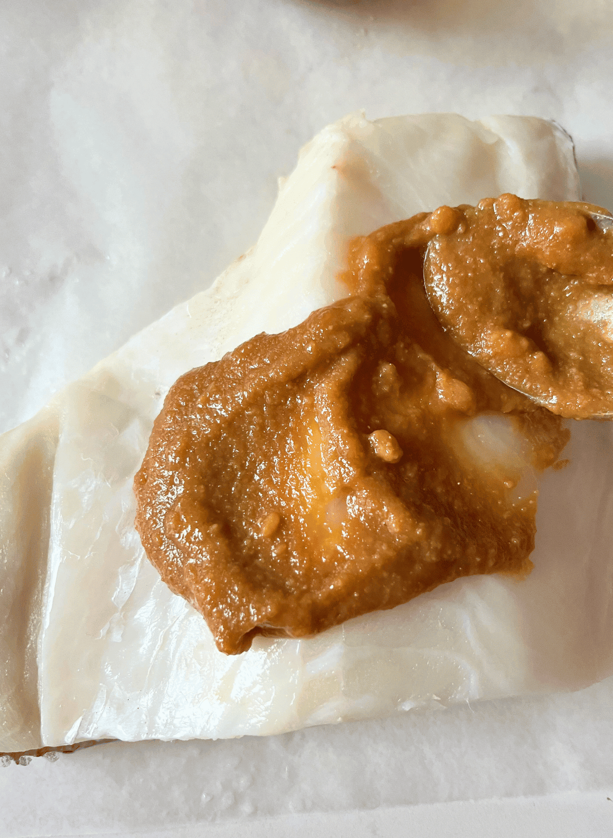 Nobu's miso paste marinade being spread on a Chilean sea bass fillet with a spoon