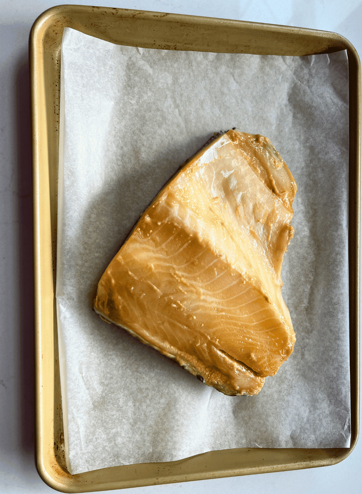 Nobu's marinated chilean sea bass uncooked on a parchment lined gold color baking sheet