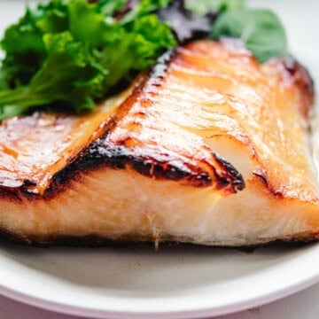 Close up shot of Nobu's Chilean Sea Bass on a white round plate with spring mix greens