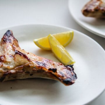 Two hamachi collars on two white round plates with lemon wedges