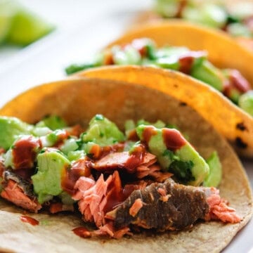 3 sockeye salmon tacos on a rectangular grey plate with 2 lime wedges