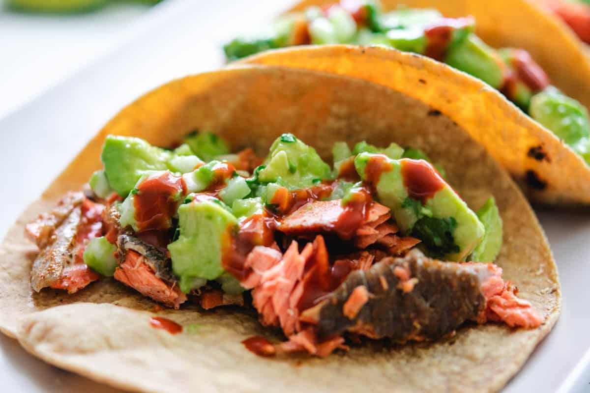 2 sockeye salmon tacos on a rectangular grey plate with 2 lime wedges