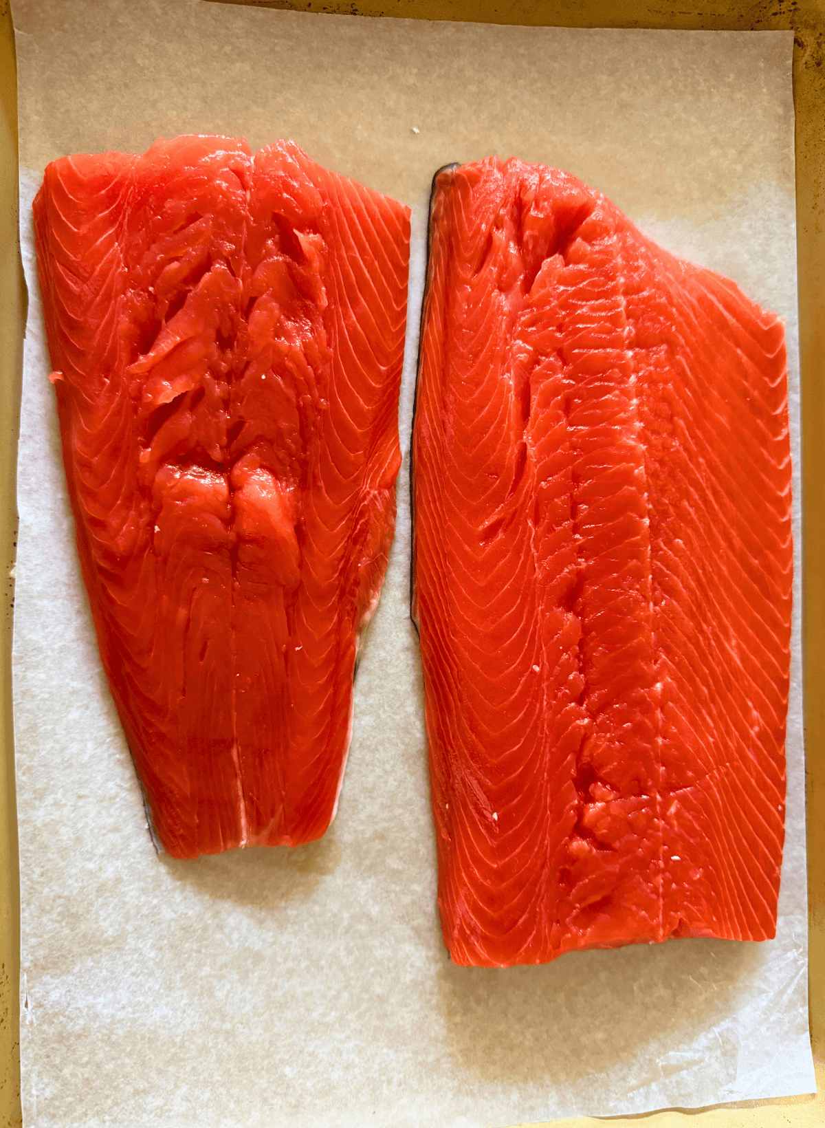2 raw fillets of sockeye salmon with lemon slices on a parchment lined gold baking sheet